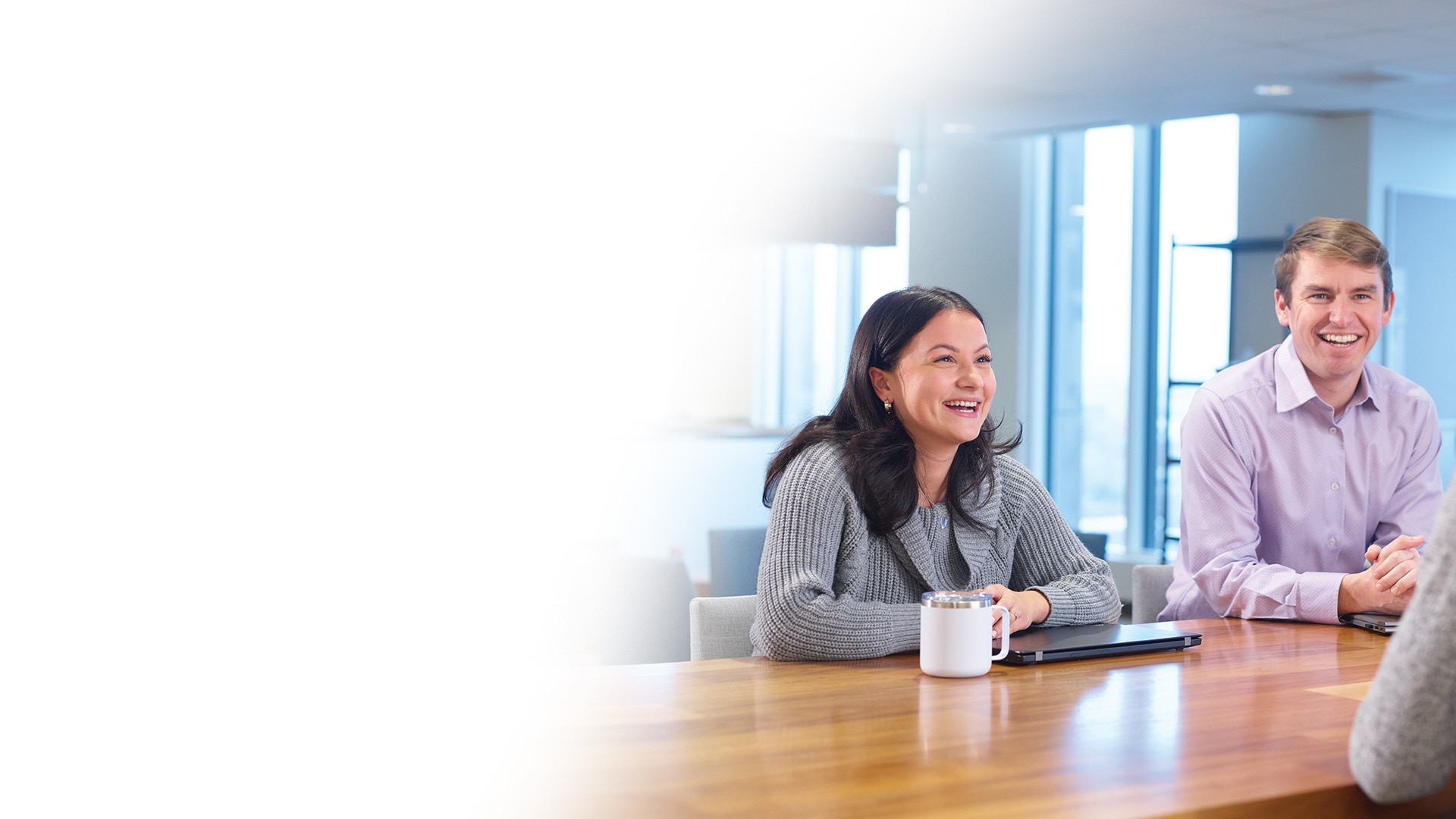 Two colleagues - man and woman - in a meeting smiling at their team