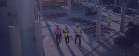 Three people in hard hats and reflective vests walking outside an office building